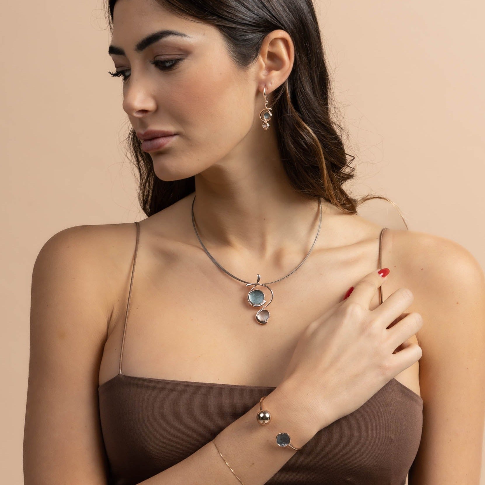Collana con cavi d'acciaio dipinti in marrone e pendente dipinto a mano con due smalti.   Lunghezza collana: 42 cm + 5 cm estensione  Altezza pendente: 4,8 cm  Materiale: zama con finitura galvanica in oro rosé  Tonalità smalti: verde, marrone