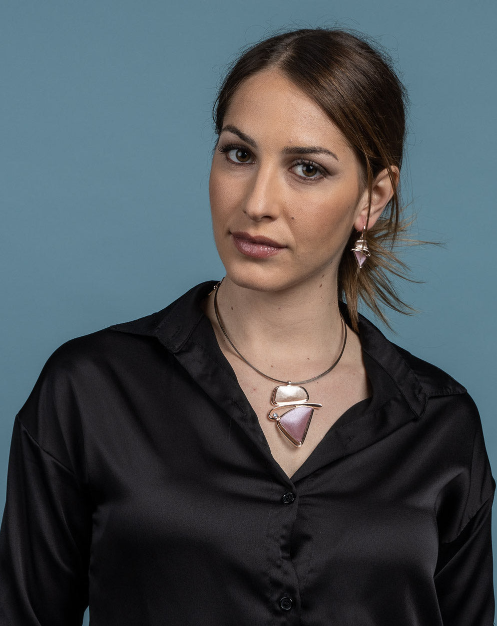 Collana con cavi d'acciaio dipinti in marrone e pendente dipinto a mano con tre smalti.   Lunghezza collana: 42 cm + 5 cm estensione  Altezza pendente: 6 cm  Larghezza max pendente:  4,5 cm  Materiale: zama con bagno in oro rosé  Tonalità smalti: beige, rosa, azzurro