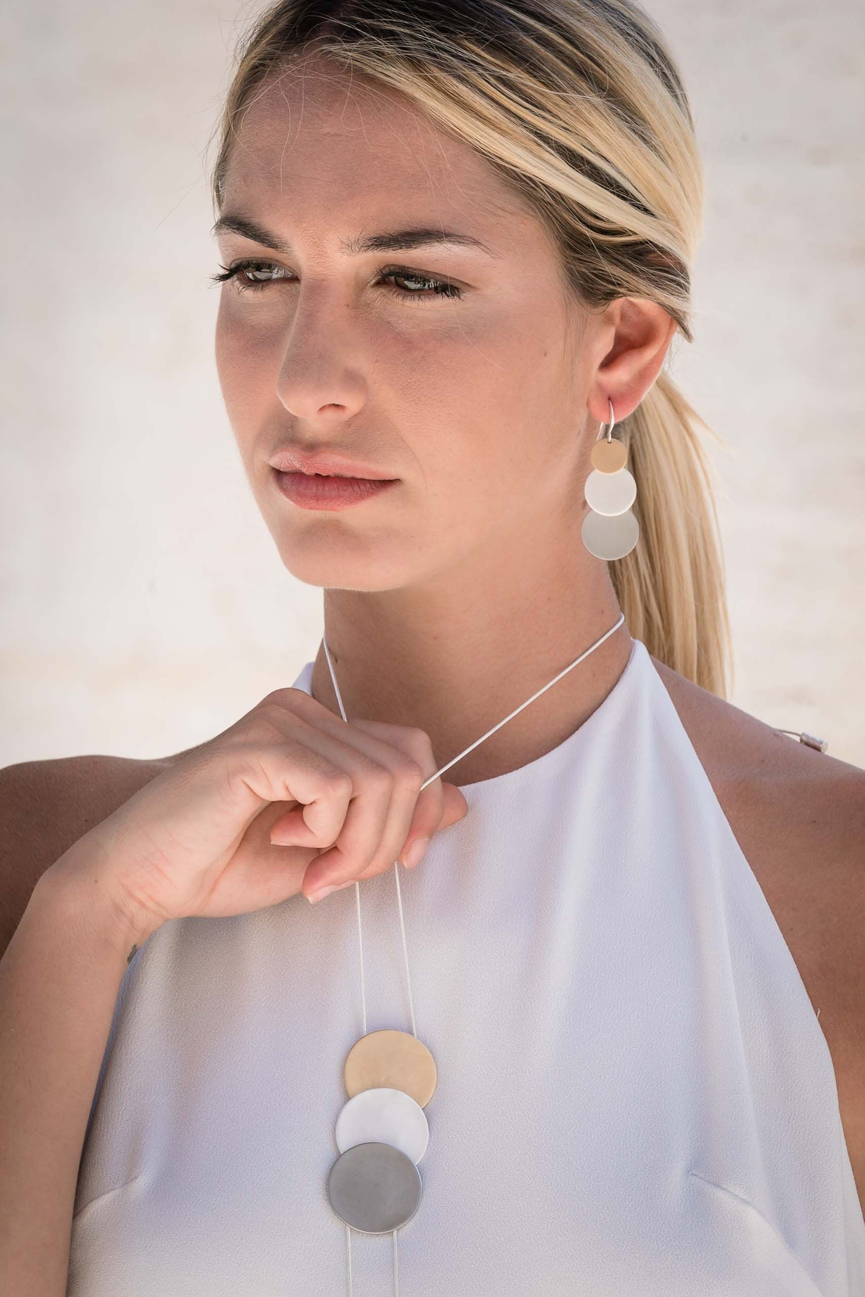 Collana lunga regolabile con tre tondi in tre bagni diversi. Lunghezza: 84 cm (regolabile)  Altezza tre tondi: 7,2 cm  Materiale: zamak con bagno in argento, rodio e oro. Foto con modella. Collezione Venere di KLK.